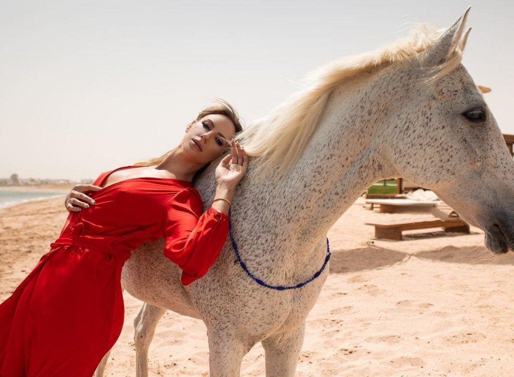 Леся Никитюк в красном платье облокотилась на лошадь
